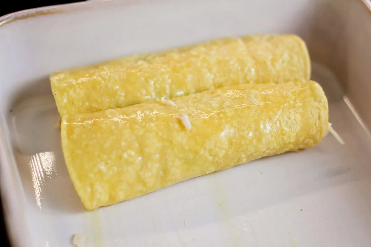 Rolled chicken enchiladas in baking dish.