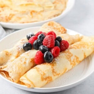 Swedish pancakes recipe rolled and topped with berries on white plate.