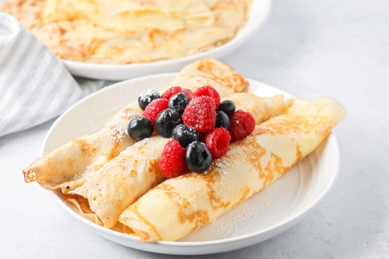 Swedish pancakes recipe rolled and topped with berries on white plate.