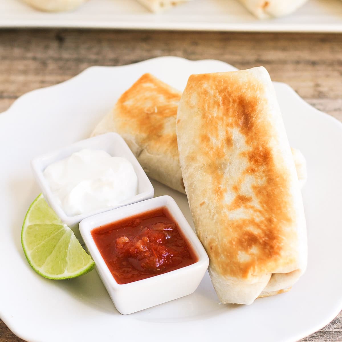 Two bean chimichangas on a plate with sour cream and salsa