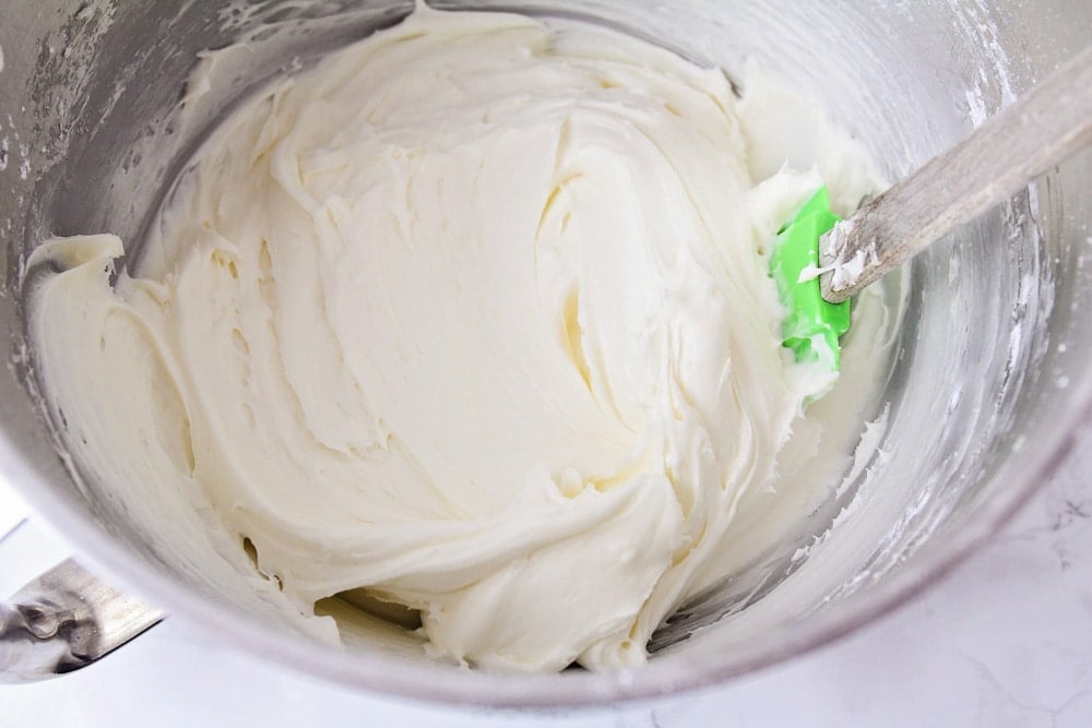 A mixing bowl filled with sugar cookie frosting, with a green rubber spatula in it.