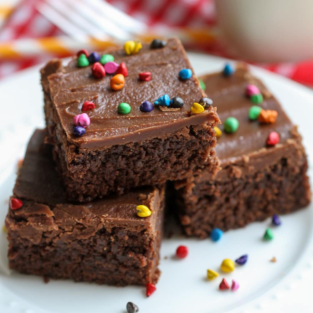 Frosted brownies stacked on white plate.