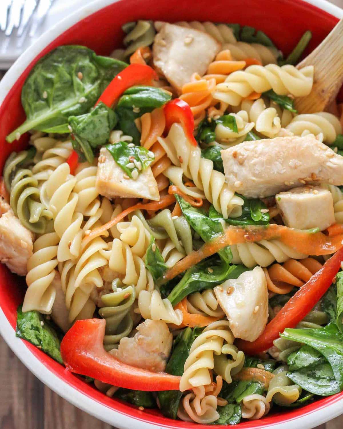 Asian Pasta salad topped with veggies in a white and red bowl