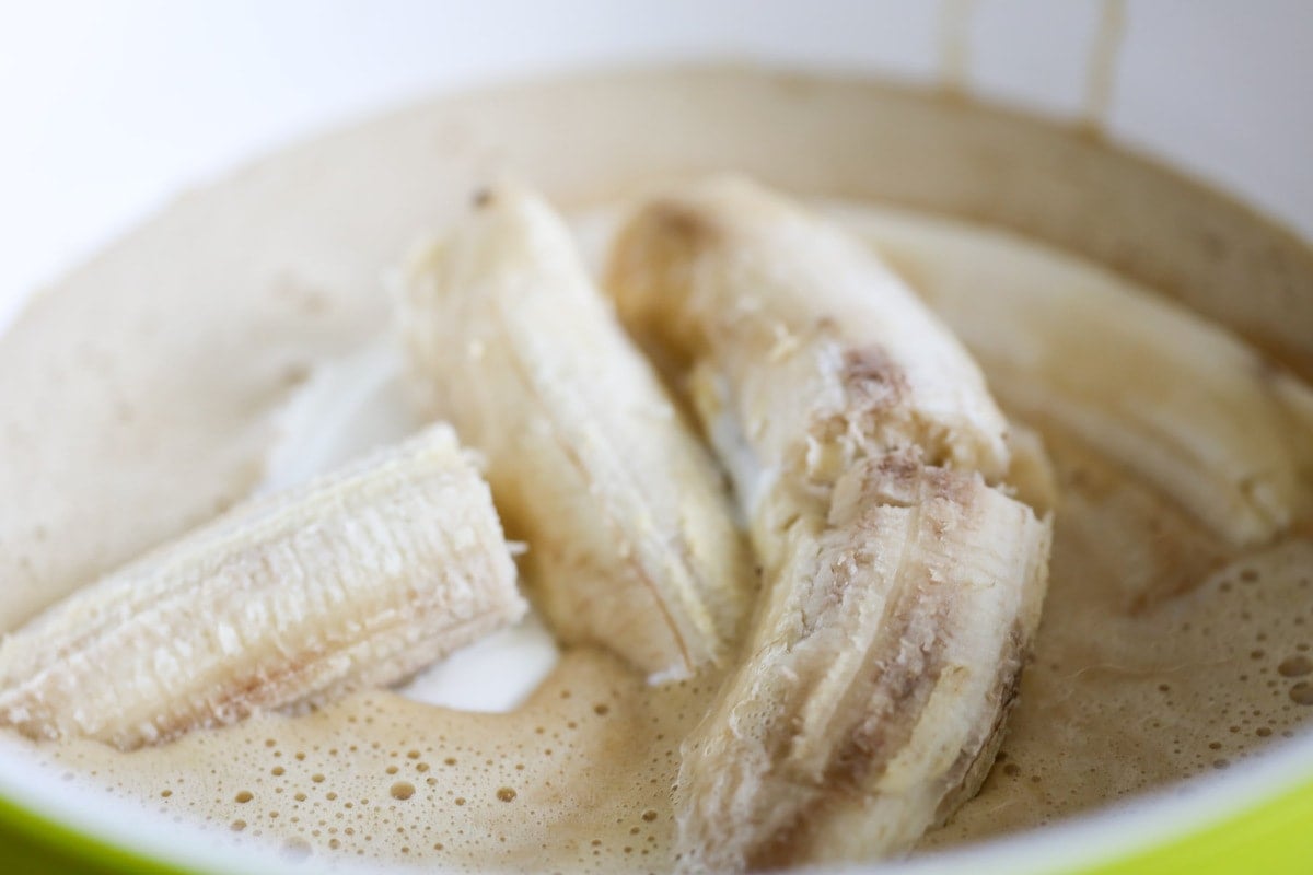 Four ripe bananas in a mixing bowl with batter.