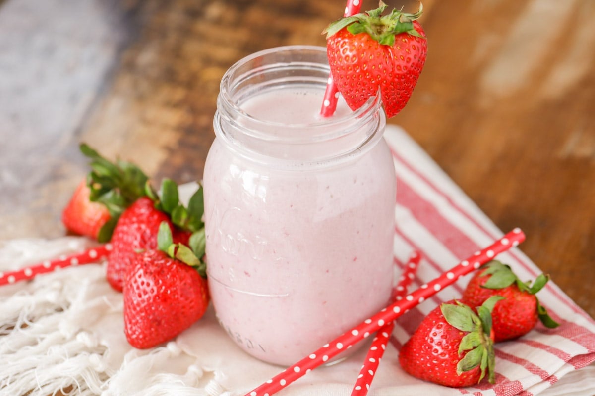 Valentines Dinner Ideas - a pudding milkshake in a Mason Jar garnished with a whole strawberry and a red straw with white polka dots. 