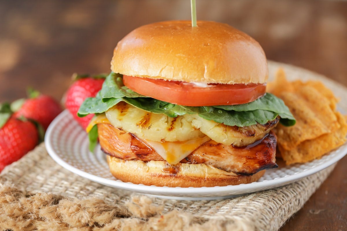 Grilled dinner ideas - a grilled teriyaki chicken burger on a white plate with chips and fruit.