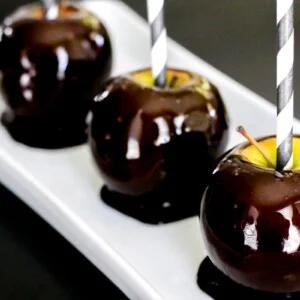 Three blackout candy apples served on a white platter.
