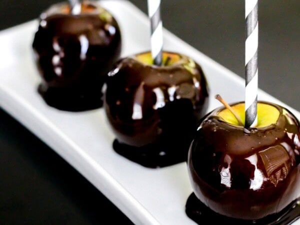 Three blackout candy apples served on a white platter.