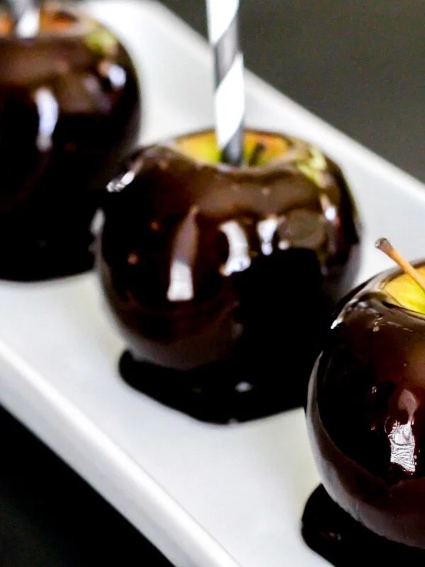 Three blackout candy apples served on a white platter.