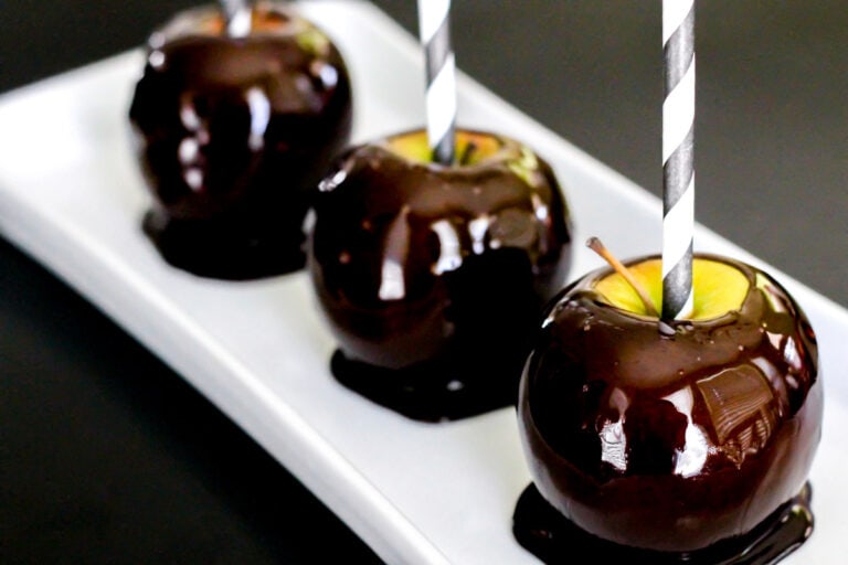 Three blackout candy apples served on a white platter.