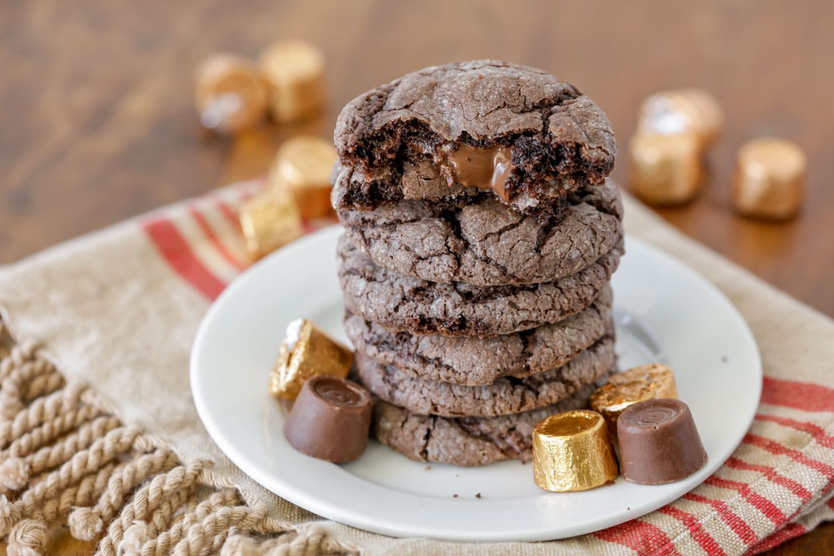 Gooey rolo cookies stacked on a plate surrounded by rolo candies.
