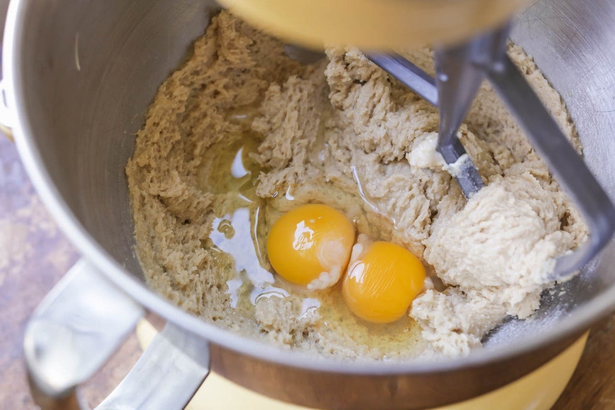 Adding eggs to a cookie batter in a bowl.