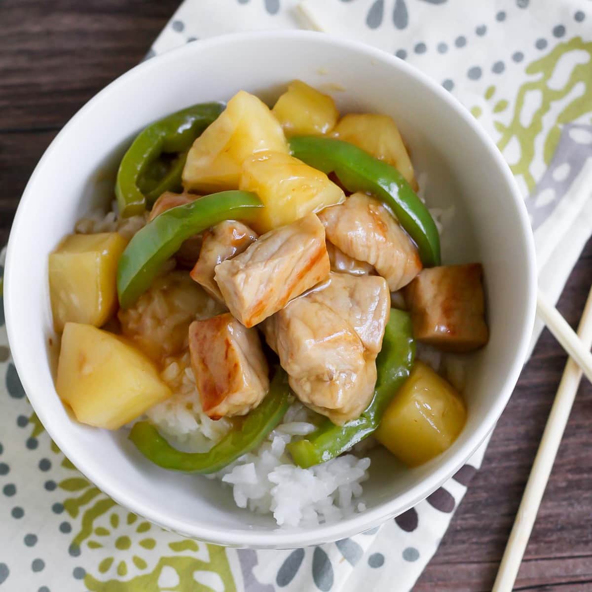 Sweet and Sour Pork with peppers and pineapple over rice in a white bowl