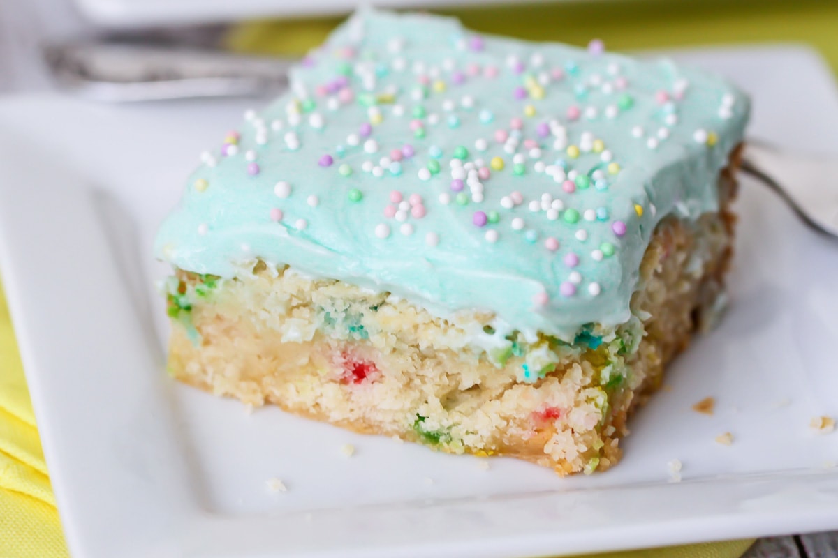 Slice of funfetti blondies covered in blue frosting and sprinkles