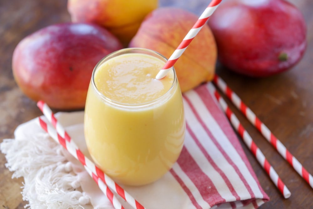 A glass of peach mango smoothie with a red and white straw.