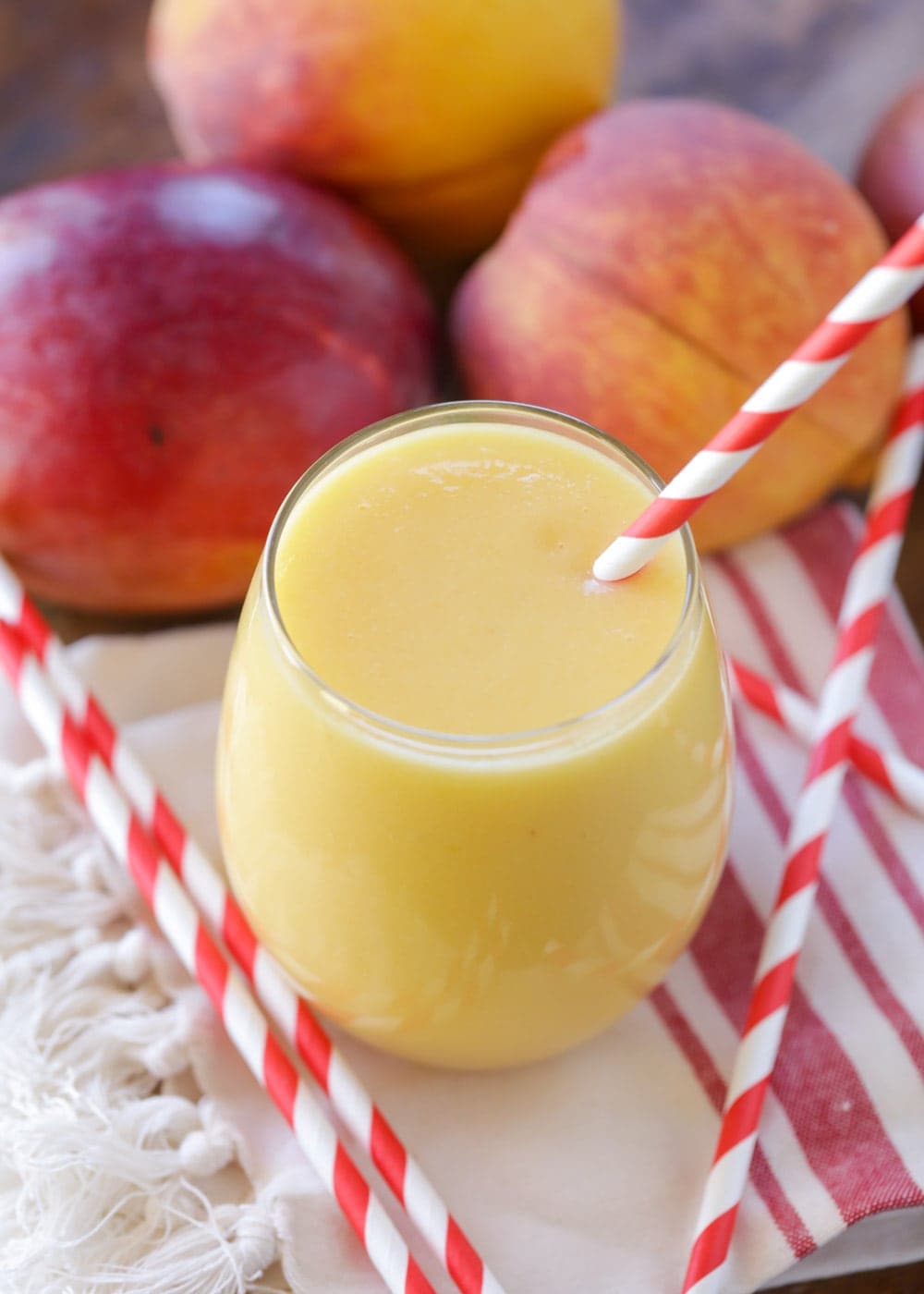 Peach smoothie - mango peach smoothie in a glass with a red and white straw.