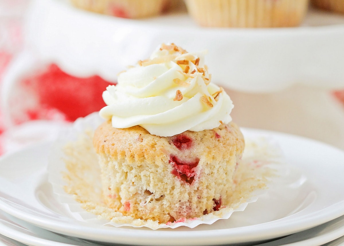 Fresh Strawberry Cupcake on white plate topped with cream cheese frosting.