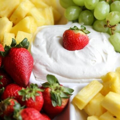 cream cheese marshmallow fruit dip on platter with strawberry on top with other fruits around it
