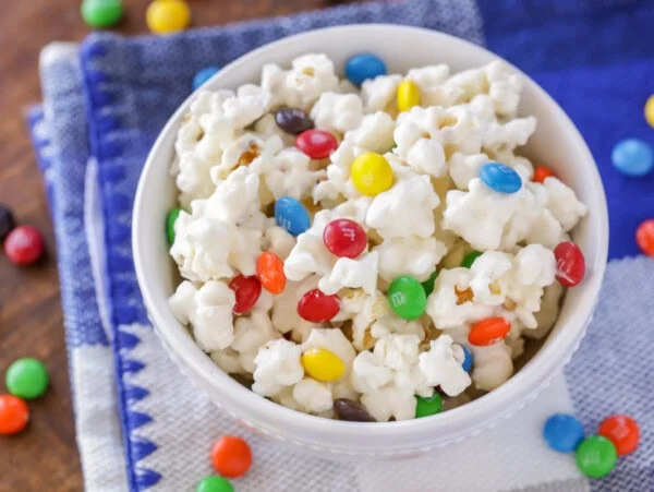 White chocolate popcorn with M&Ms in white bowl.
