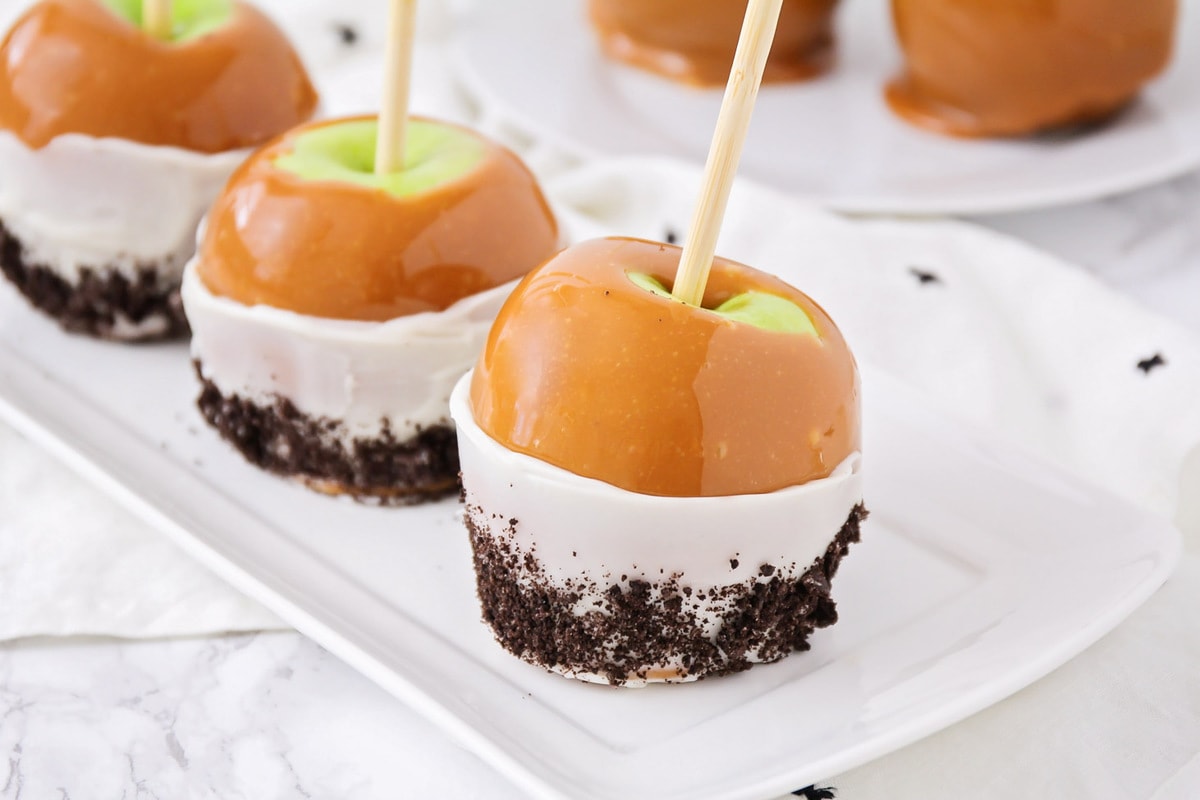 Homemade caramel apples on a white serving tray.