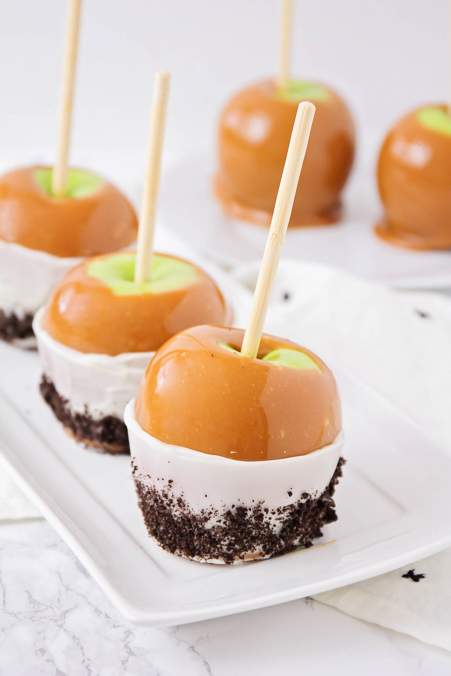 Caramel apples dipped in white chocolate and crushed Oreo lined up on a platter.