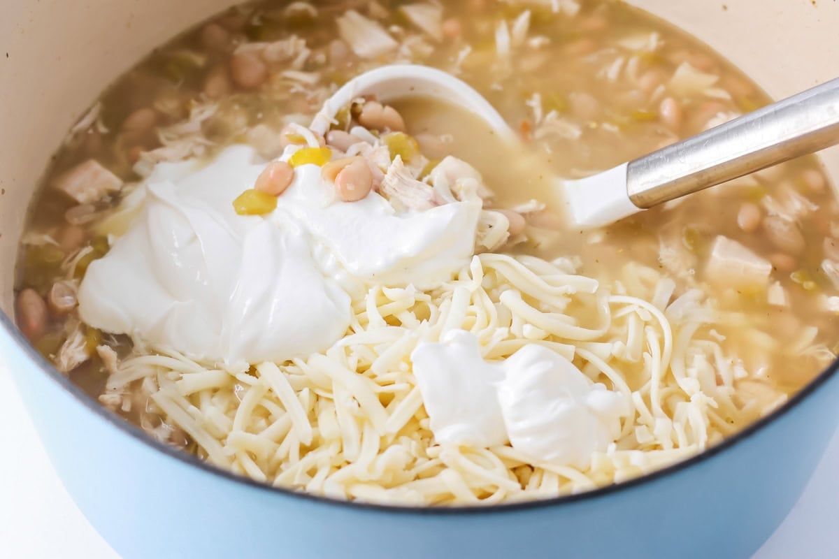 Adding sour cream to chili in large pot.