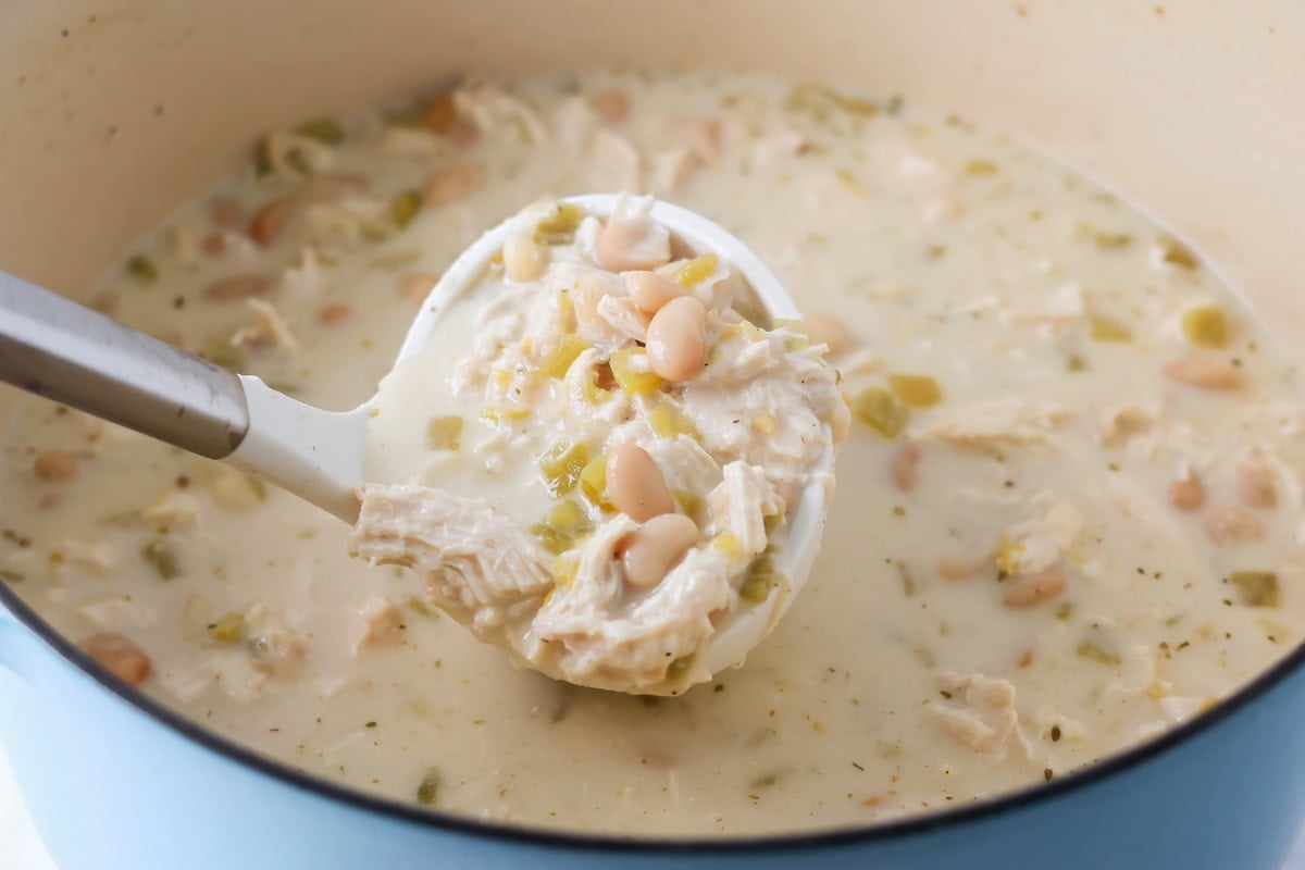 Scoop of white chicken chili being lifted out of pot.