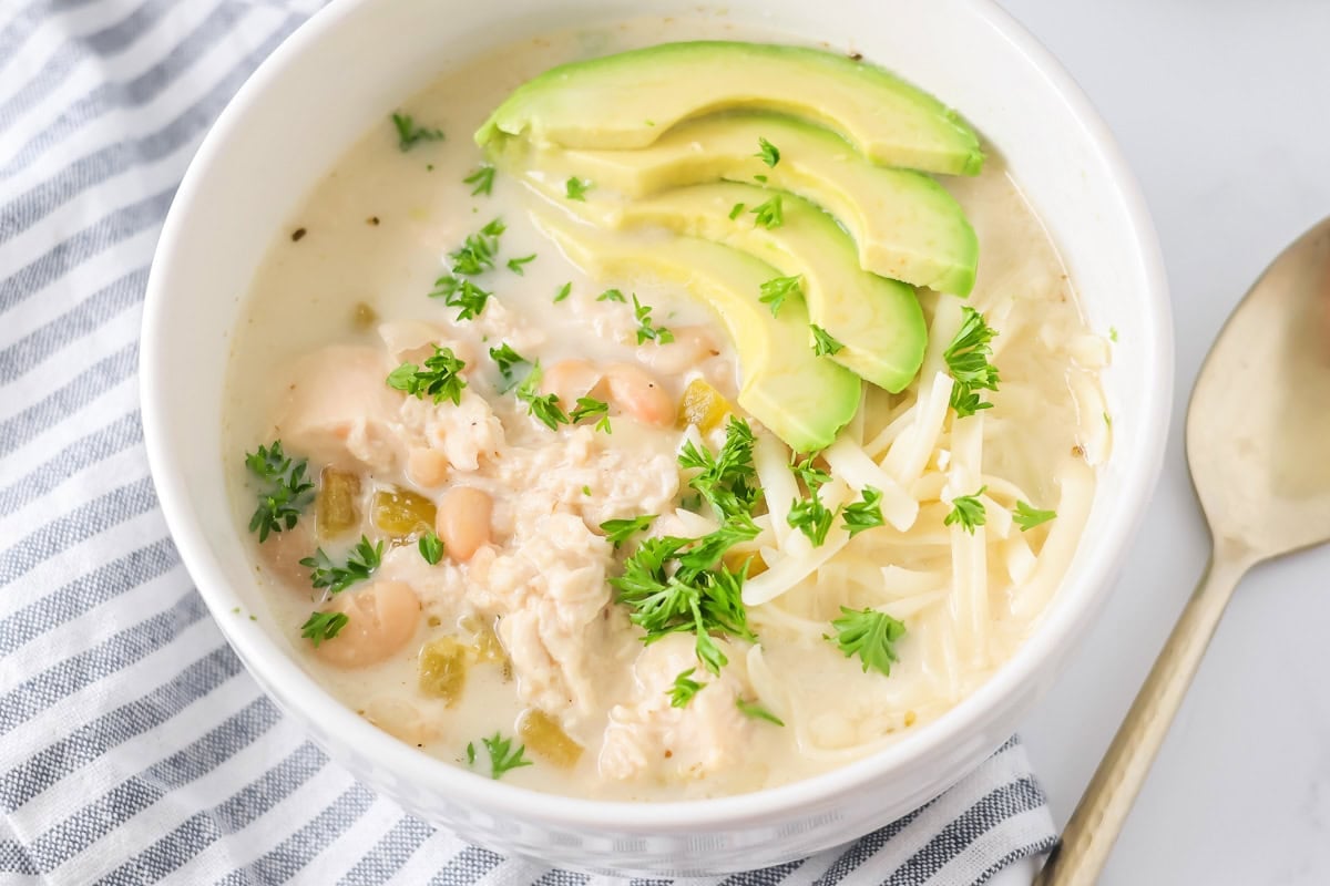 This award-winning white chili recipe with chicken is a hearty, creamy favorite!! Best of all, it's ready in 30 minutes or less! White chicken chili recipe in bowl close up image with avocado slices on top.