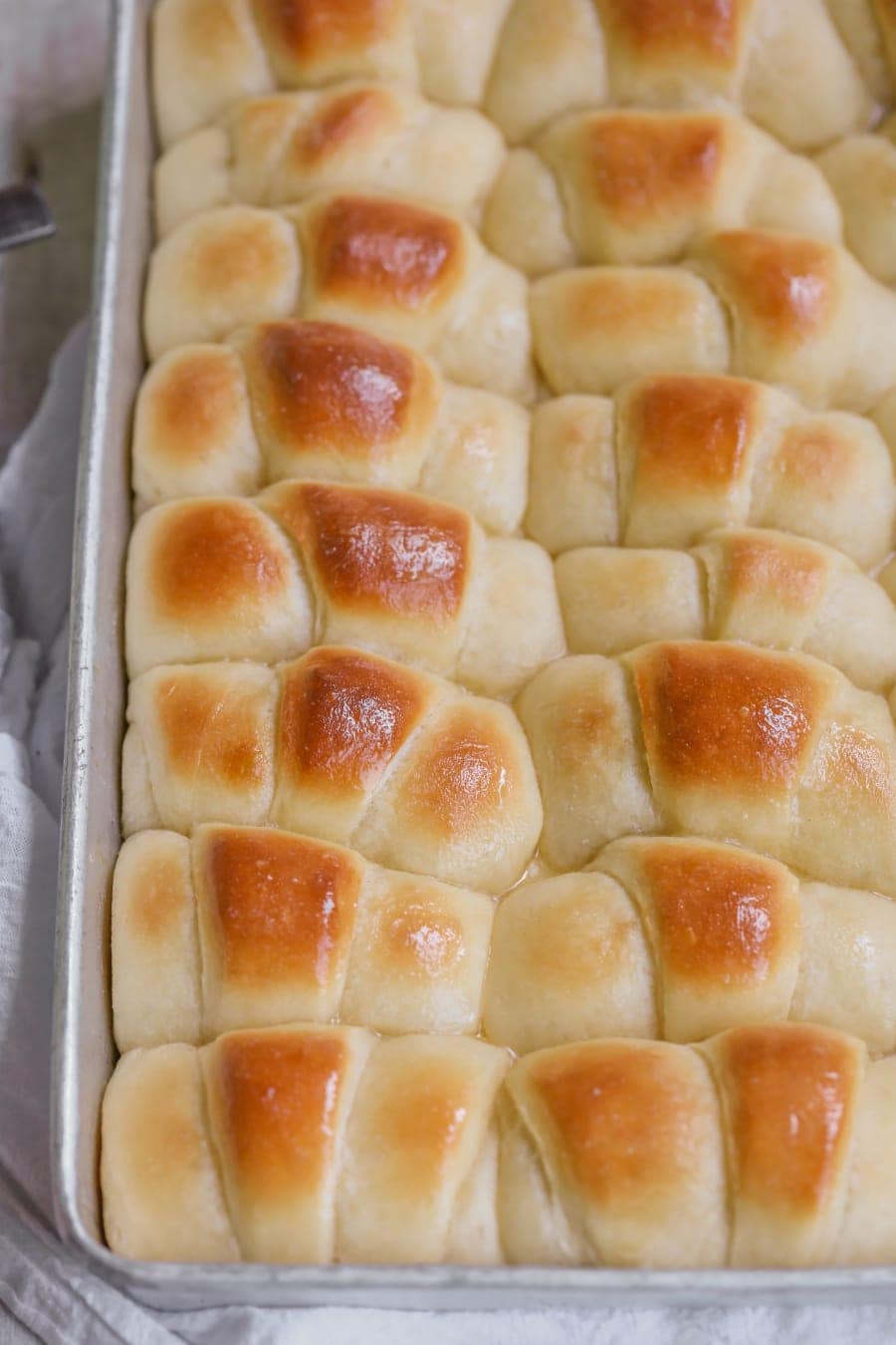 Baked and buttered homemade dinner rolls in a baking pan.