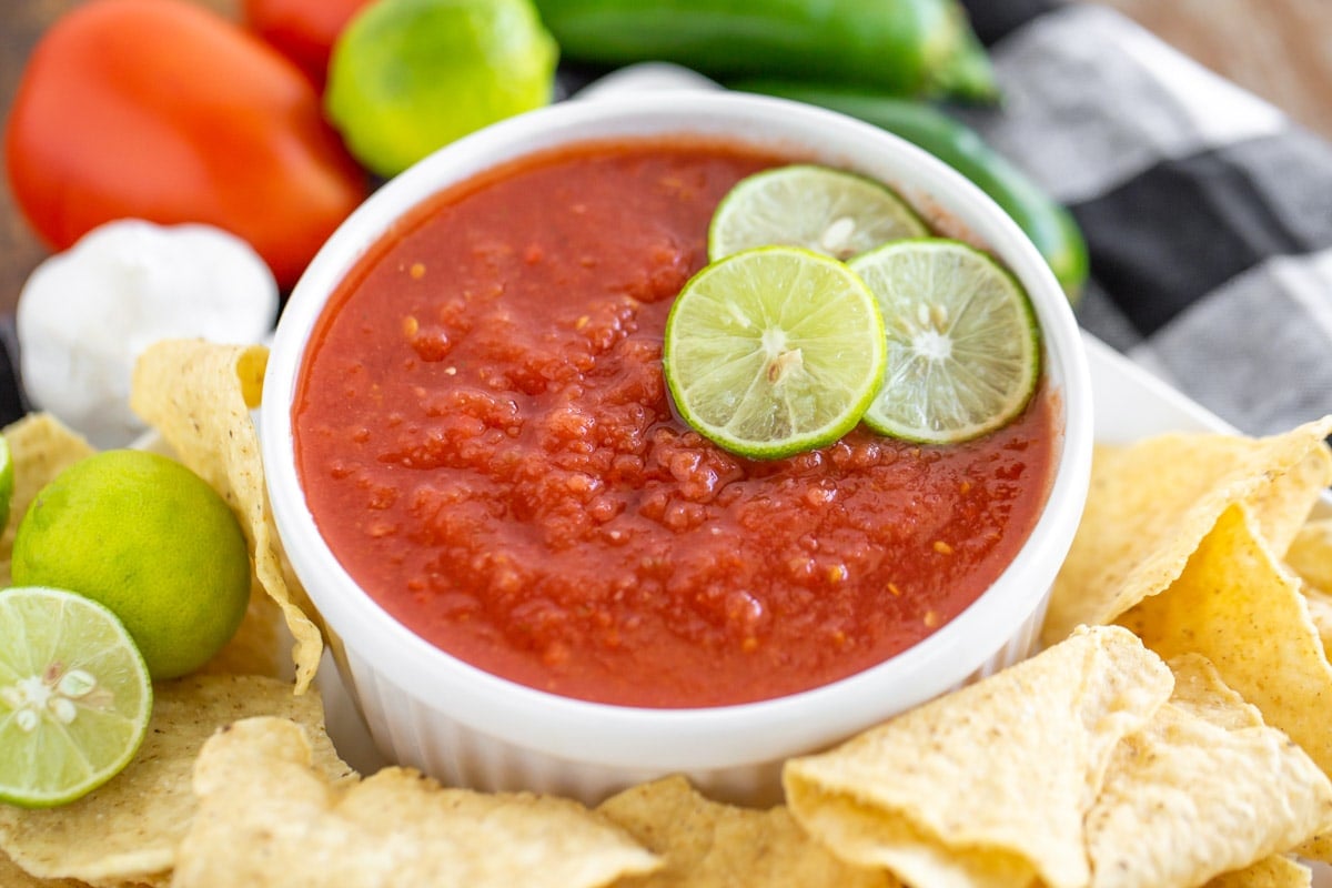 Copycat Chili's salsa in a white bowl served with tortilla chips and lime wedges.