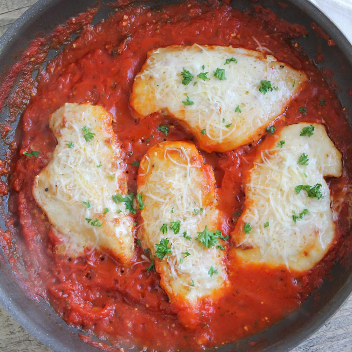 Chicken Parmigiana being cooked in crushed tomatoes in pan