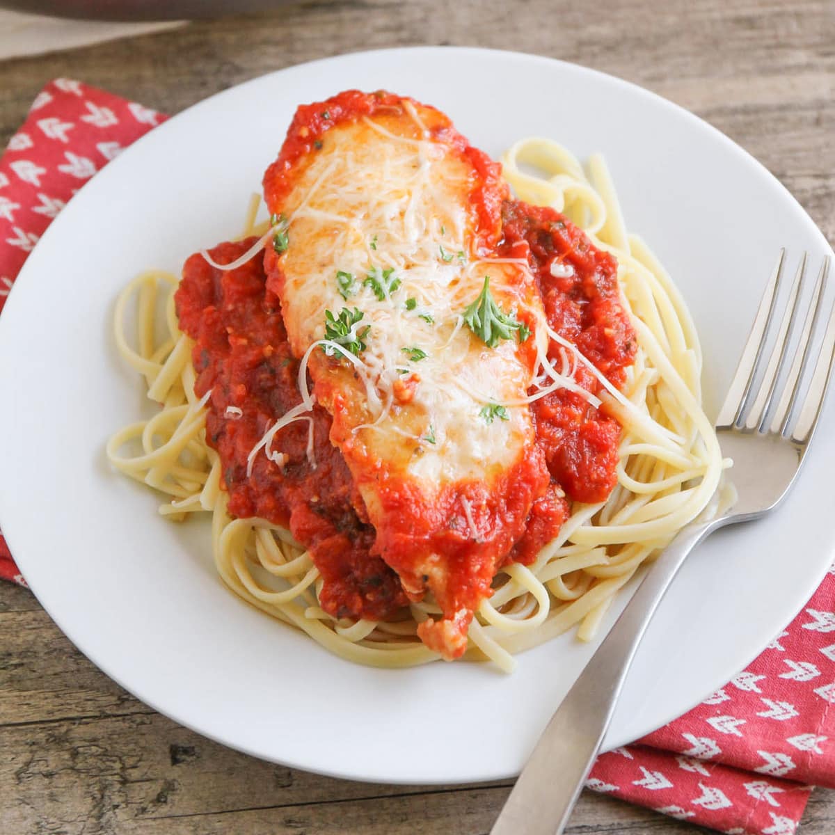 Chicken parmigiana close up served on a white plate on top of linguine pasta.