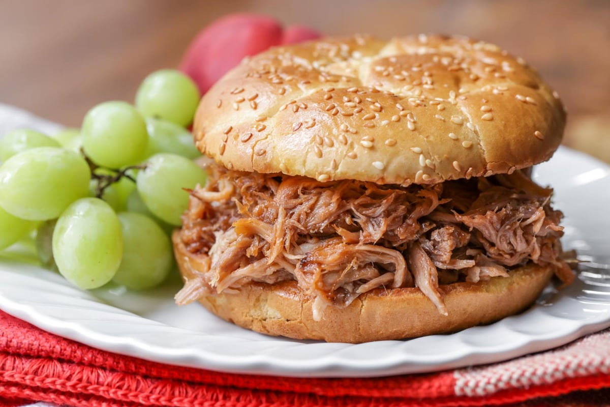 3 Ingredient Pulled Pork served on a hamburger bun with a side of green grapes.