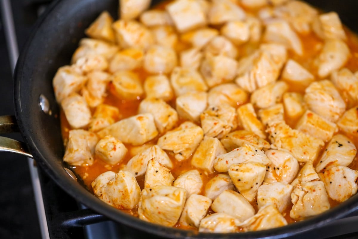 chicken simmering in buffalo sauce in a skillet