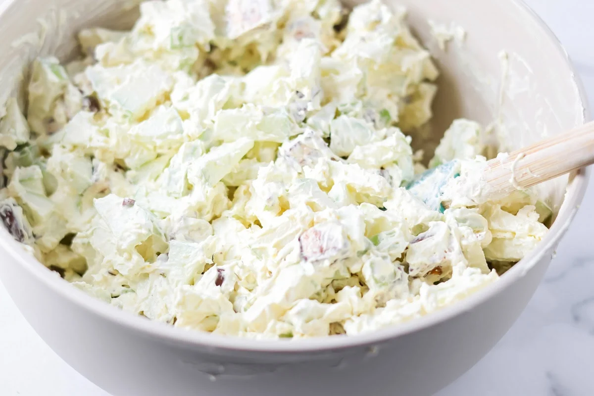 Our 10-minute Snickers salad is a sweet and tart dessert where bright pops of apples perfectly complement chewy chunks of Snickers. Snickers salad in a gray mixing bowl.