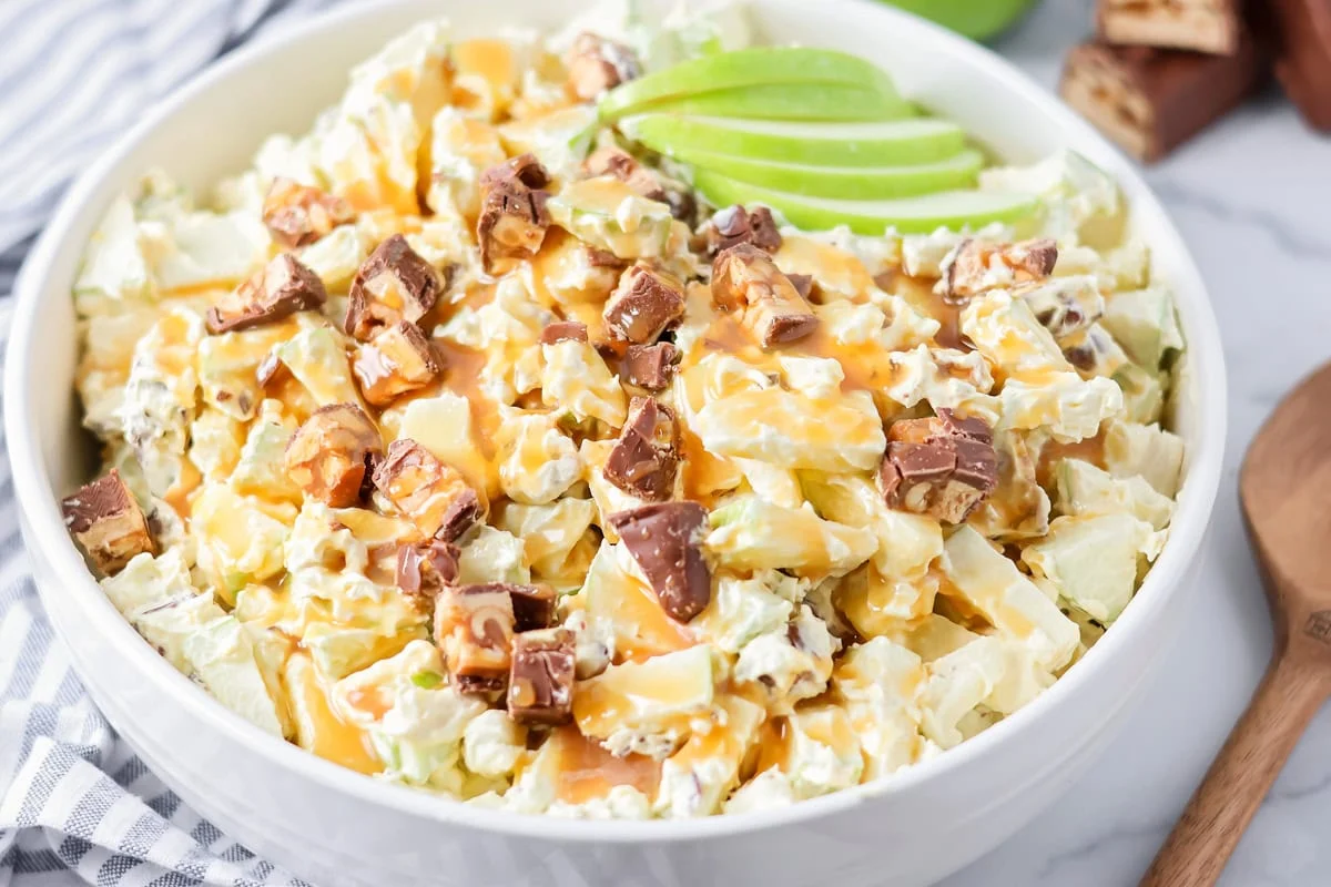 Our 10-minute Snickers salad is a sweet and tart dessert where bright pops of apples perfectly complement chewy chunks of Snickers. Snickers salad served in a large white bowl.