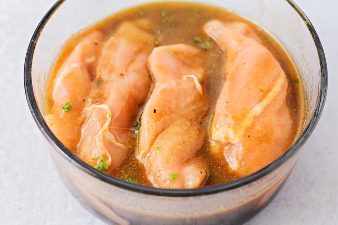 Chicken breasts in a glass bowl filled with marinade.