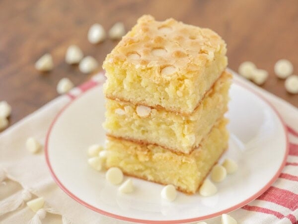 White chocolate brownies stacked on top of each other with white chocolate chips sprinkled around.