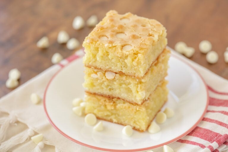 White chocolate brownies stacked on top of each other with white chocolate chips sprinkled around.