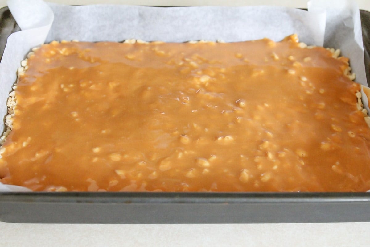 Layering caramel on top of rice krispies in a metal baking dish.
