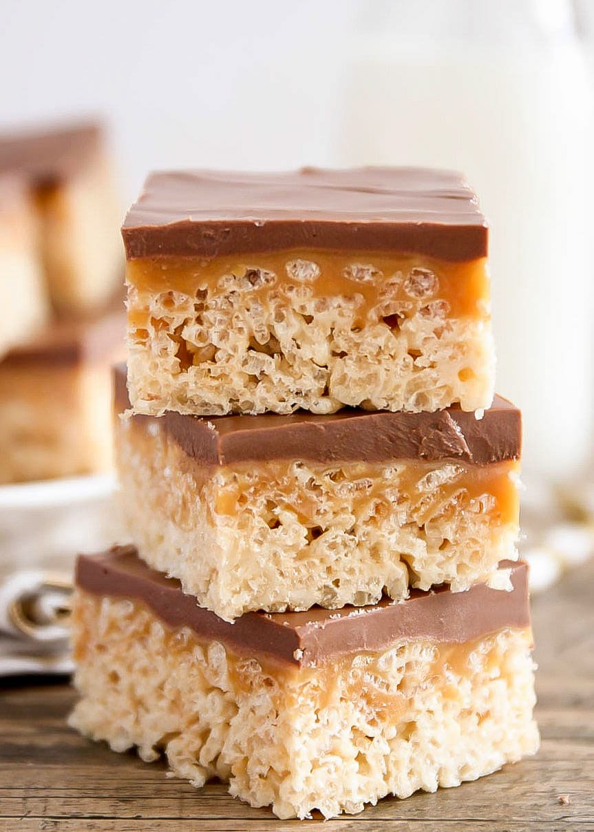 A stack of chocolate caramel rice krispie squares on a wooden table.