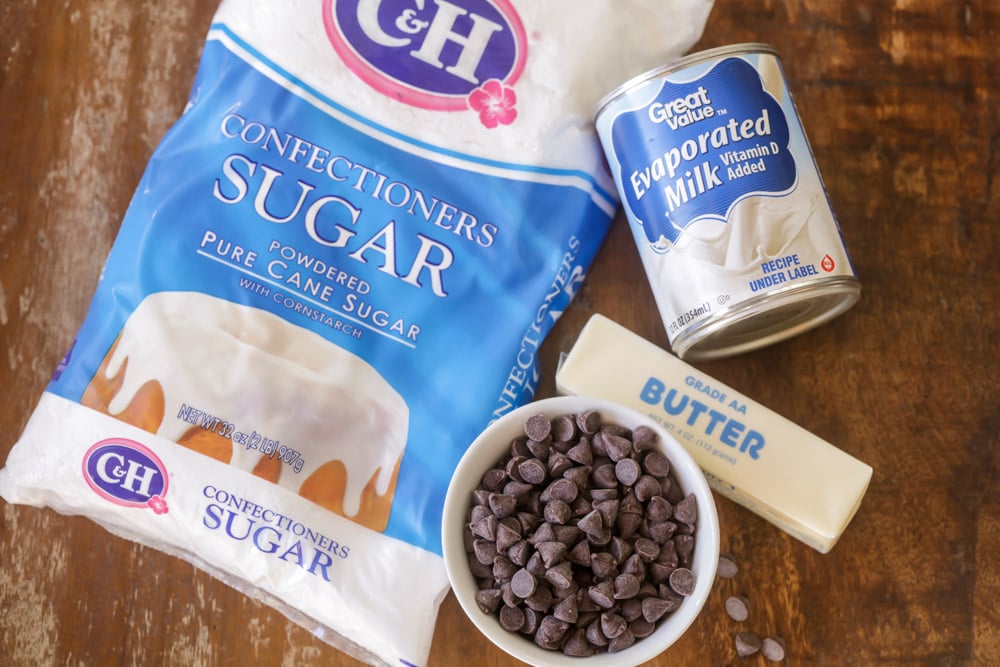 Powder sugar, evaporated milk, butter, and chocolate chips on a wooden counter.