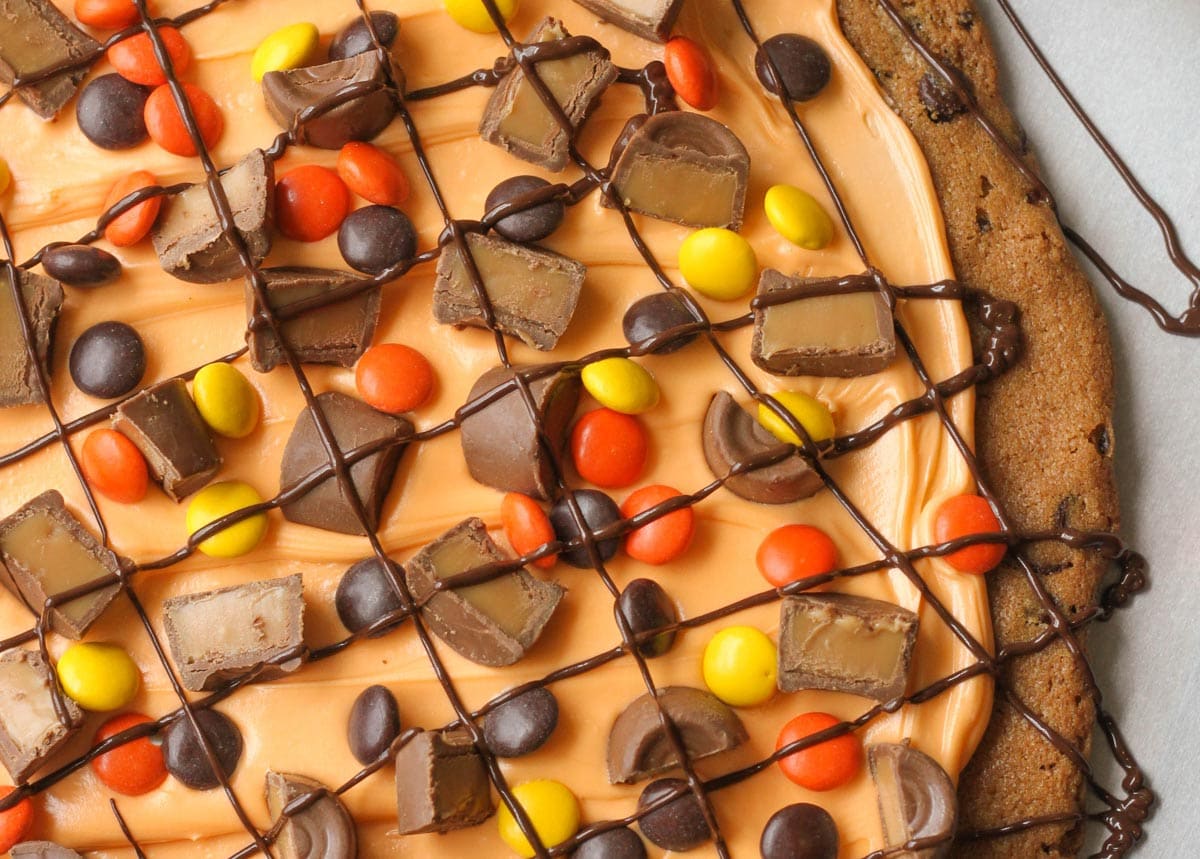Halloween dinner ideas - orange Halloween cookie cake topped with candy pieces and chocolate drizzle.