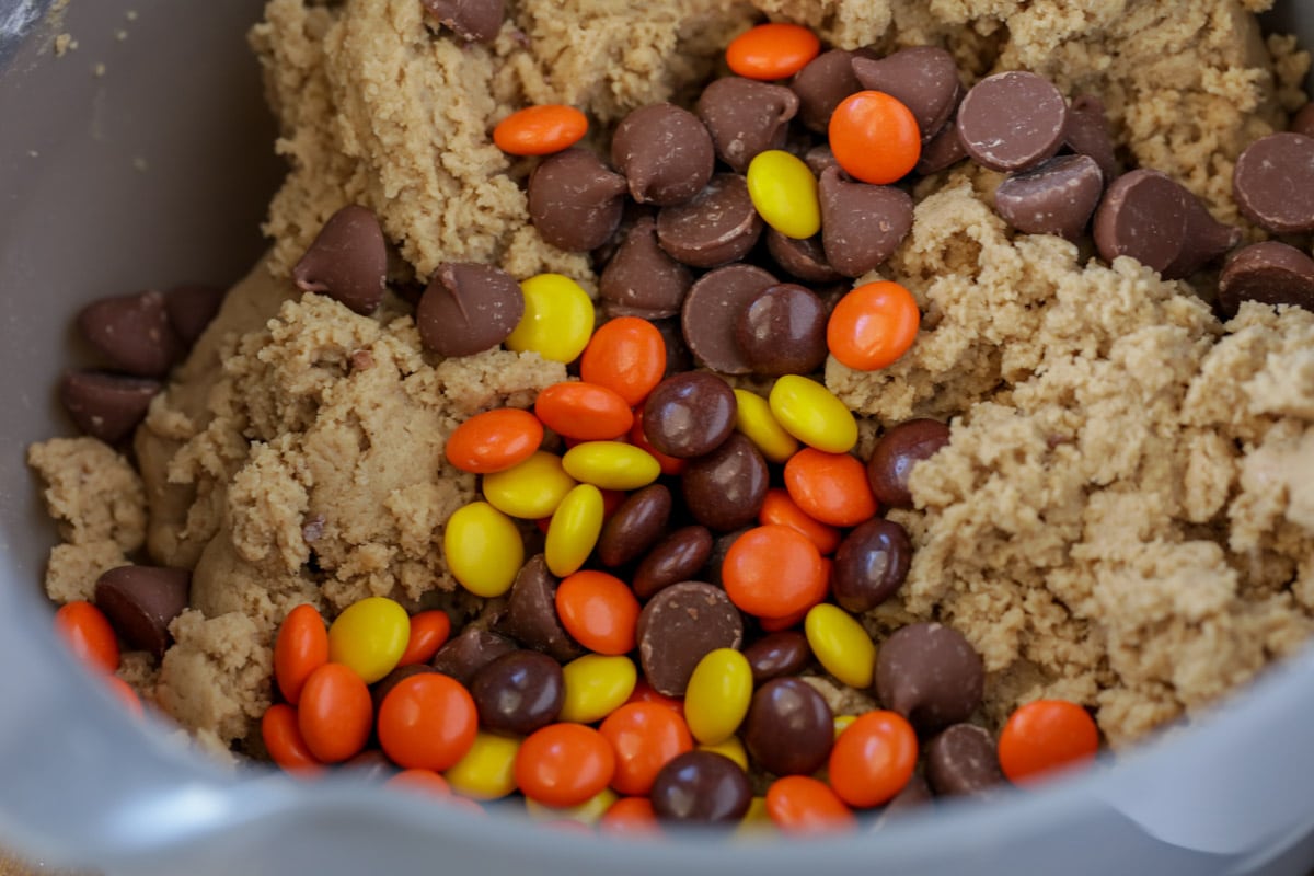 Batter in a bowl with chocolate chips and Reeses Pieces poured on top.