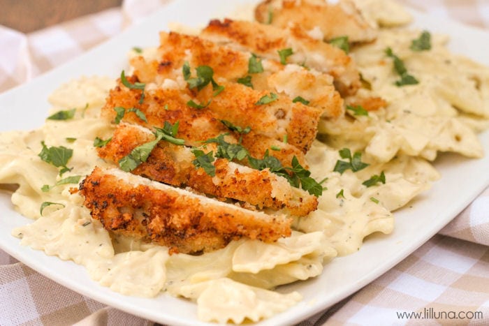 sliced crispy chicken topped with parsley on a plate of creamy pasta.