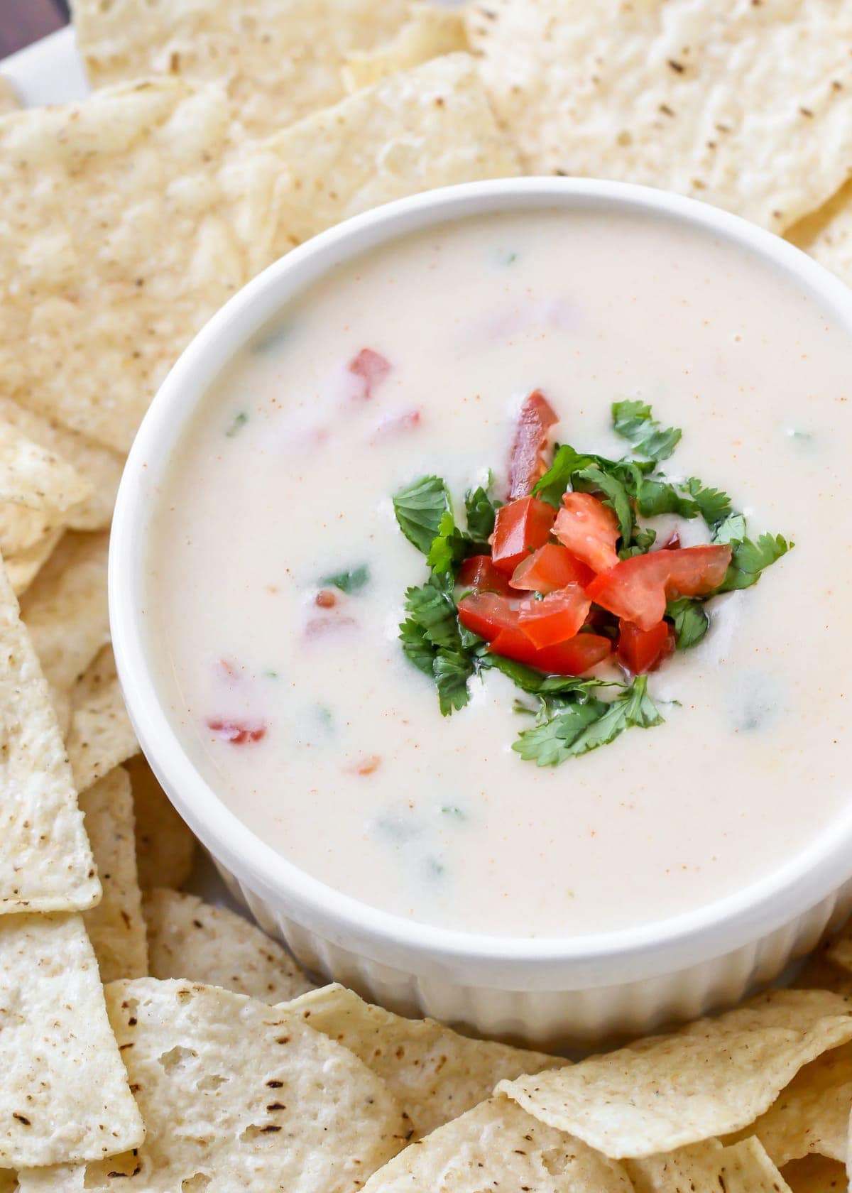 Queso Blanco dip topped with tomatoes in white bowl surrounded by tortilla chips