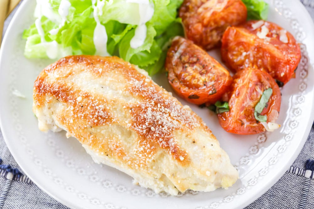 Chicken Dinner Ideas - Mayo parmesan chicken bake with salad and tomatoes on a white plate.