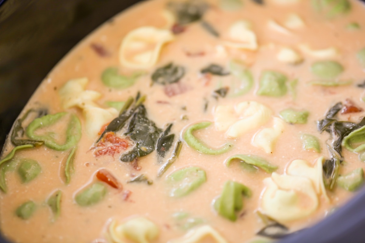 Tortellini and spinach soup inside a slow cooker.