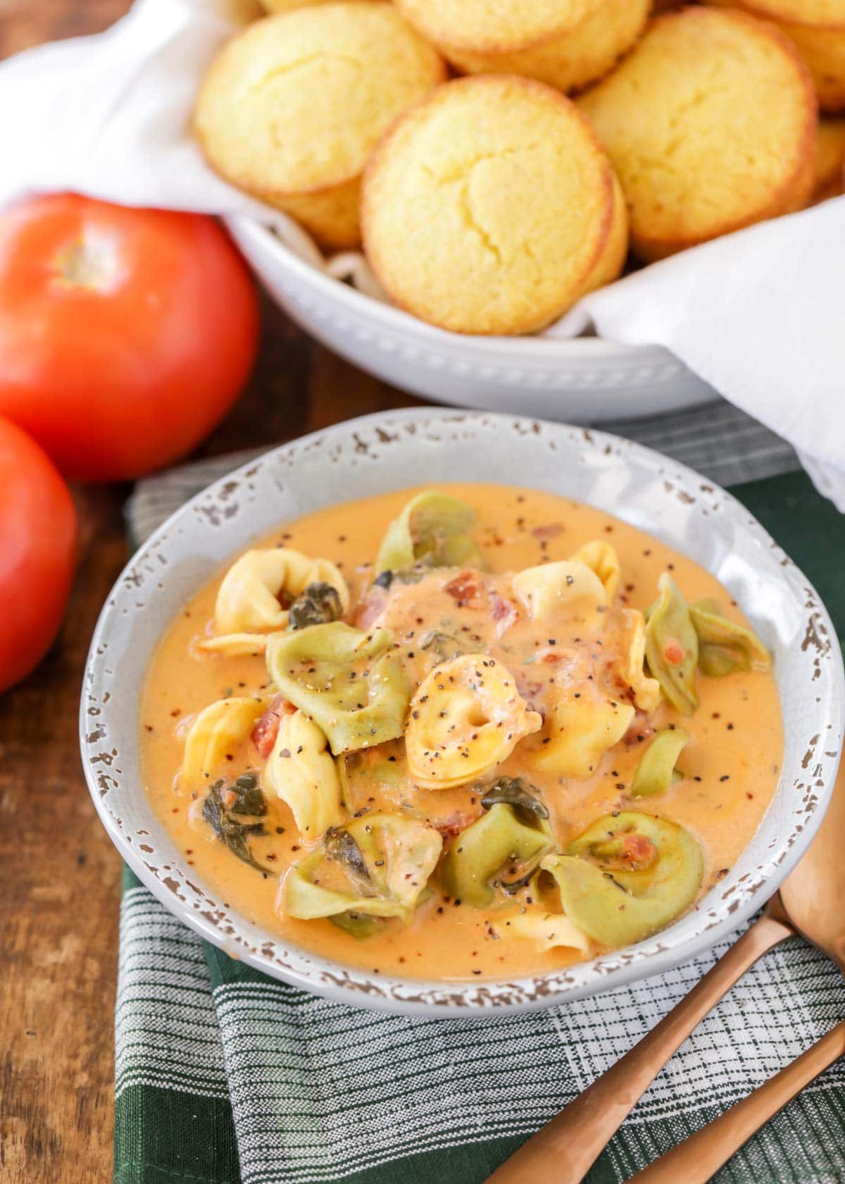 Spinach tortellini soup and cornbread served in white bowls.