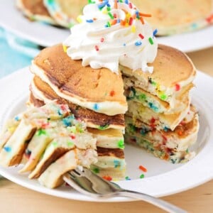 A stack of funfetti pancakes topped with whipped cream and a bite missing.